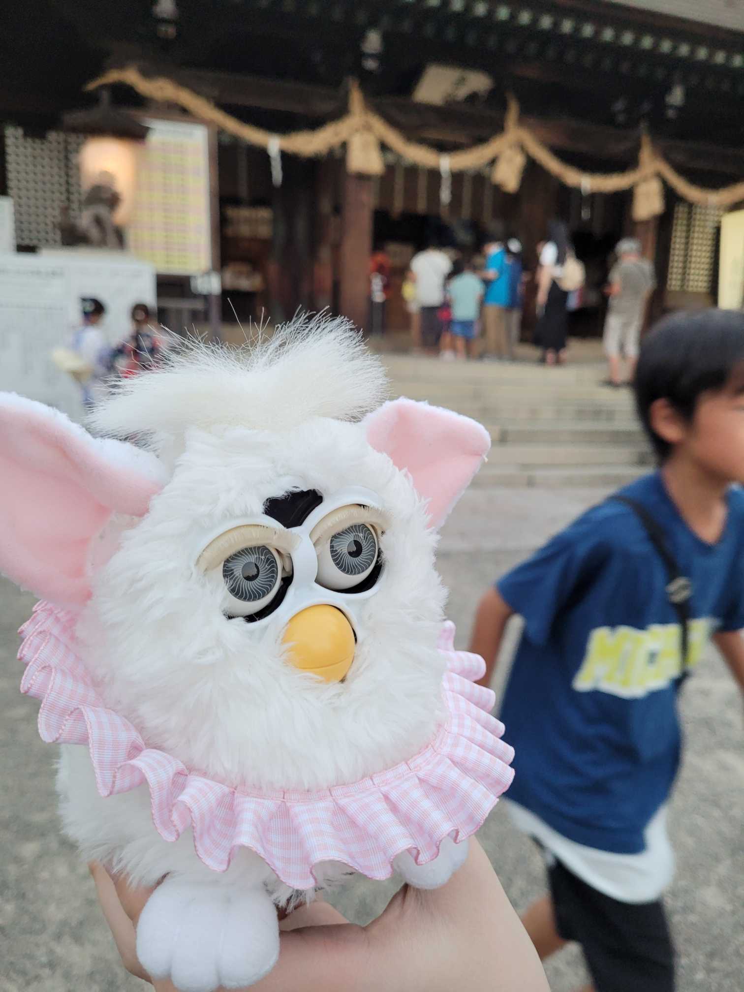 白いファービーが神社の建物の前でポーズしている